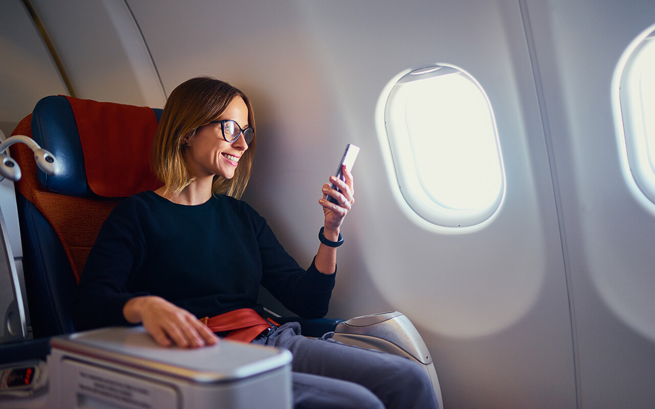 Traveling and technology. Flying at first class. Pretty young businees woman using smartphone while sitting in airplane.