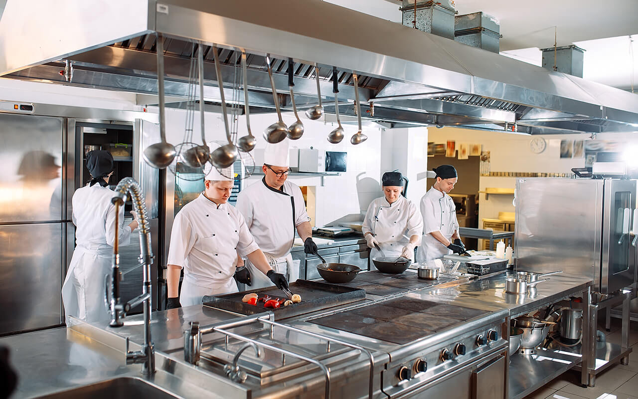 Five chefs wearing uniforms posing in a kitchen