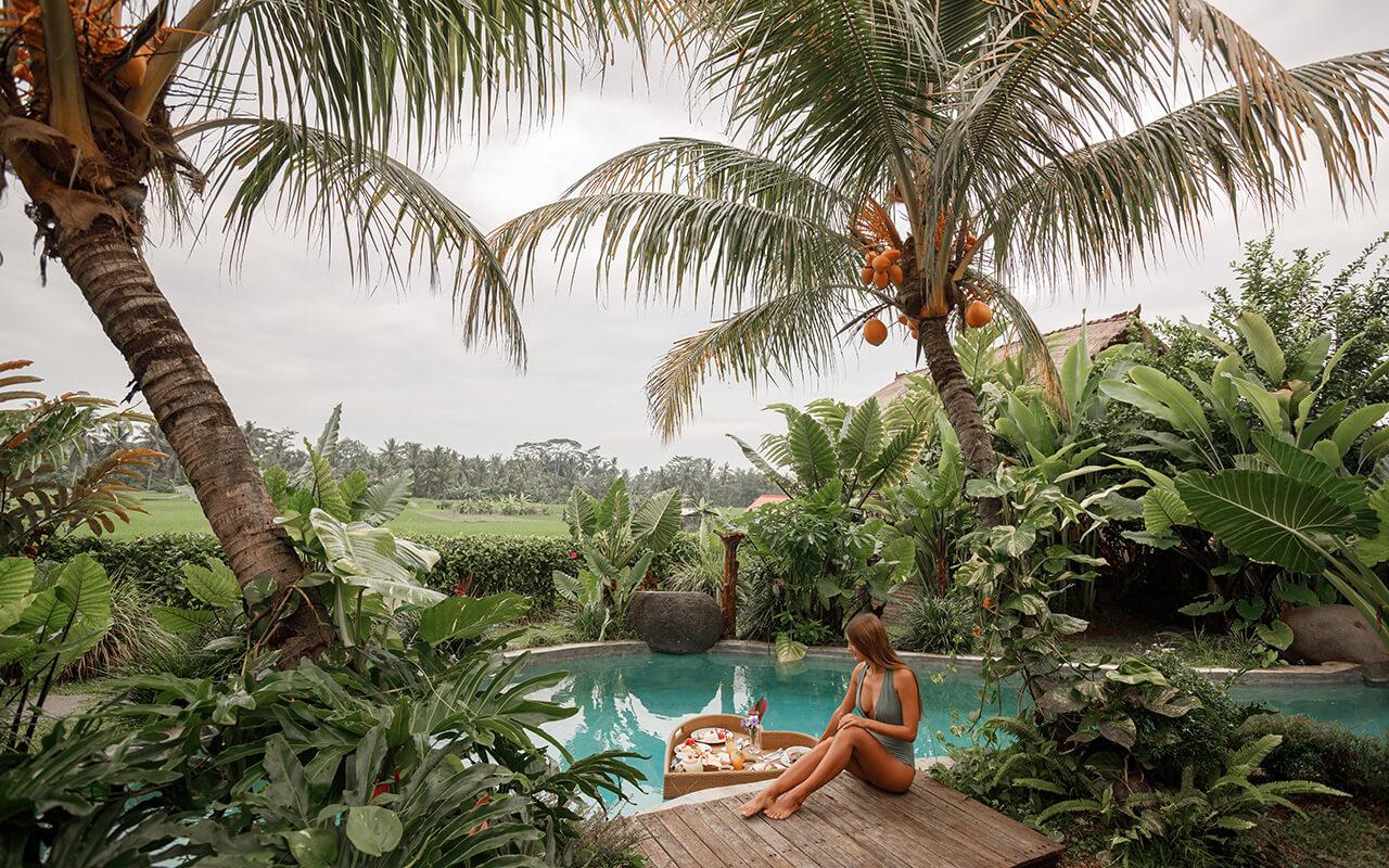 Girl relaxing and eating floating breakfast in jungle pool surrounded with palm trees on luxury villa in Bali