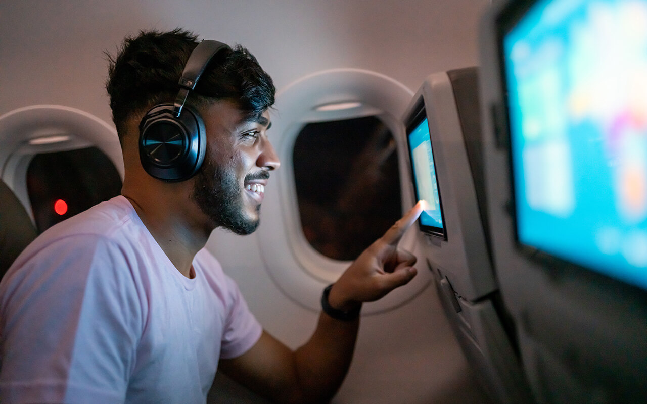 Passenger in airplane touching LCD entertainment screen.