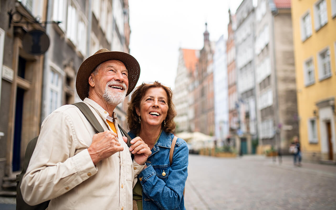 Portrait of happy senior couple tourists outdoors in historic town