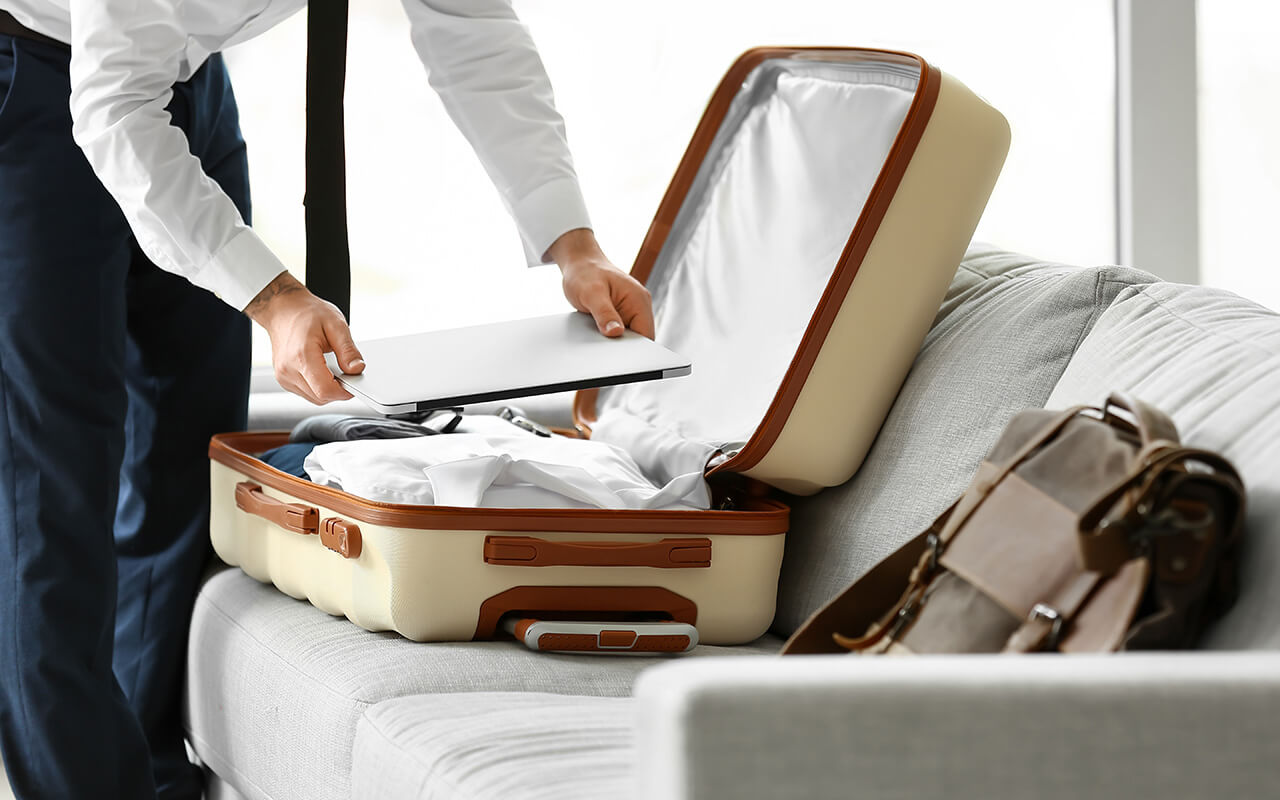 Man putting a laptop in his suitcase