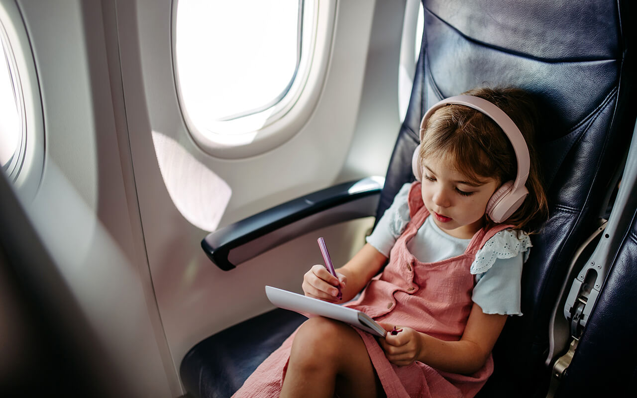 Kid with headphones drawing on an airplane