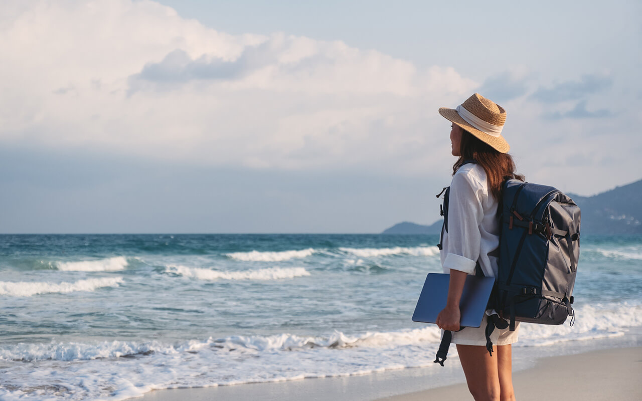 A female traveler holding laptop computer while walking on the beach