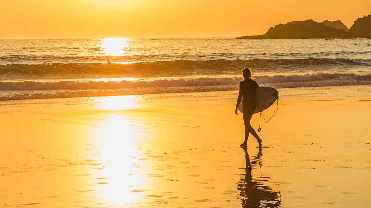 a person walking on the beach with a surfboard at sunset