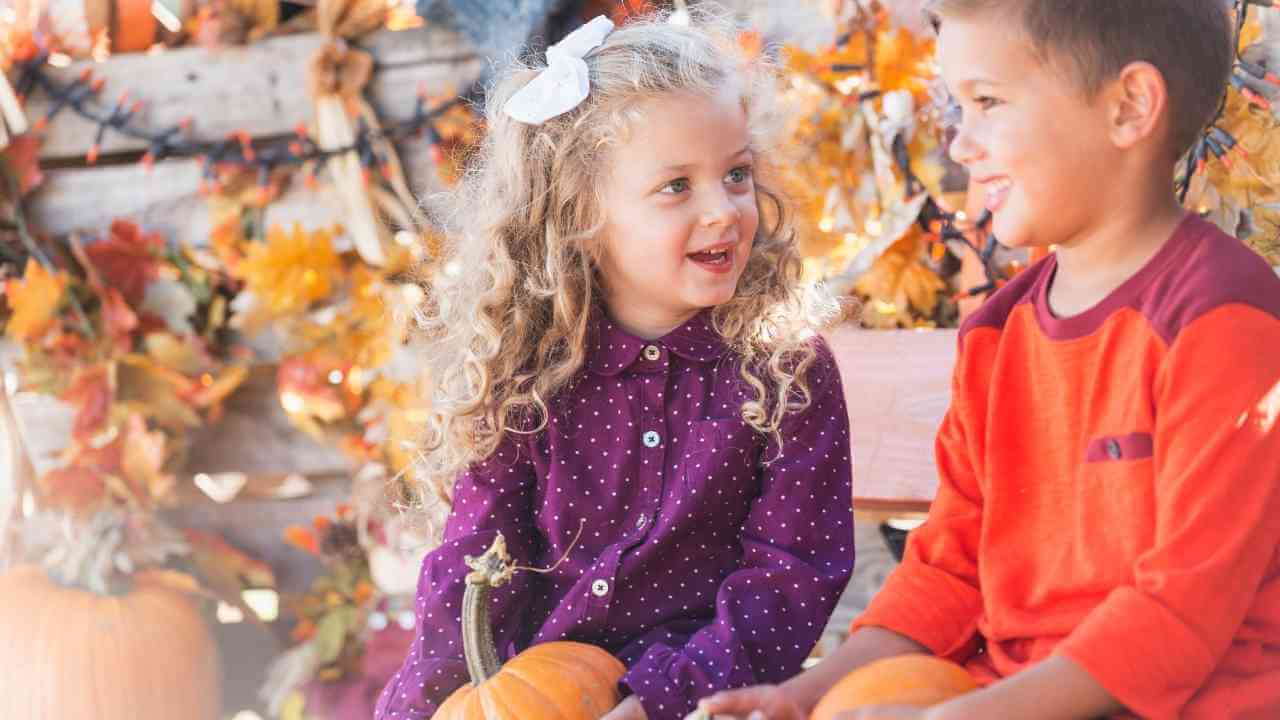 two children sitting on a bench with pumpkins