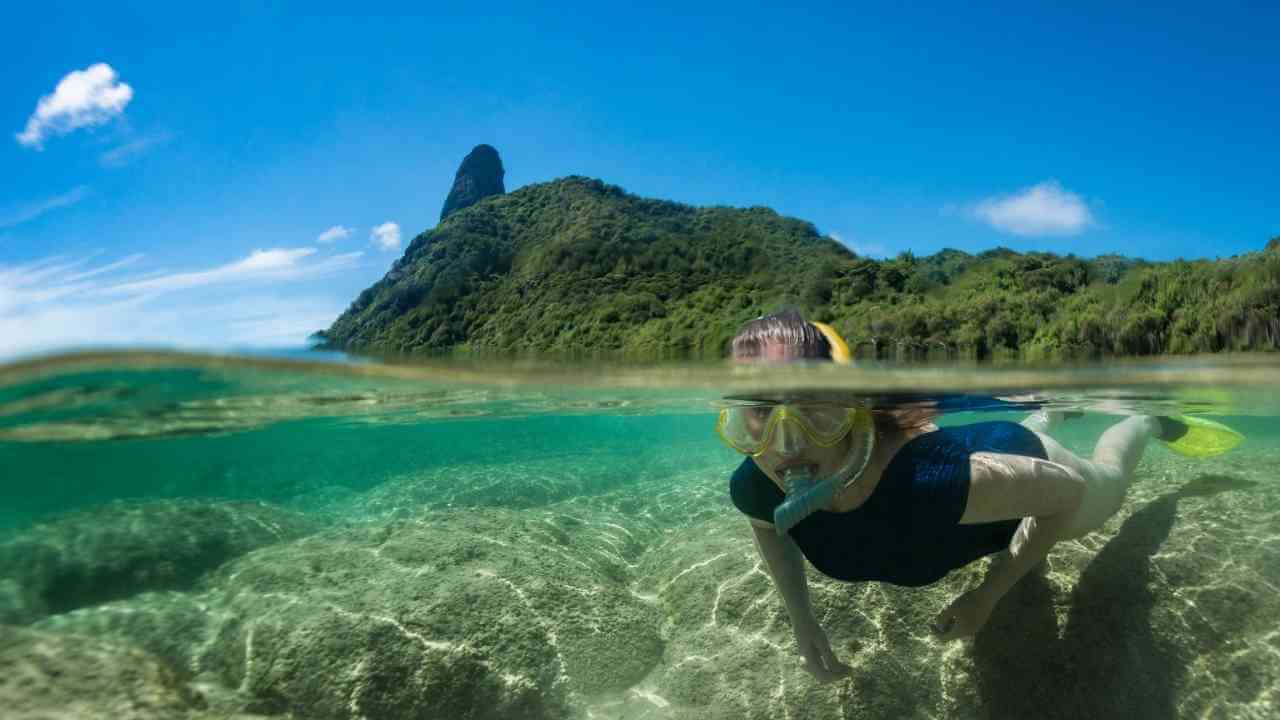 a person snorkeling in the ocean with a mountain in the background