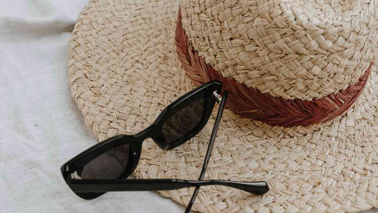 a straw hat and sunglasses laying on a bed