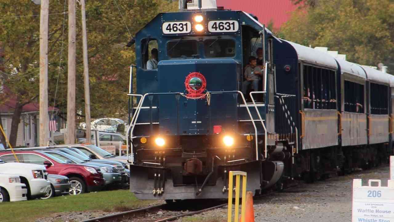 a blue train traveling down the tracks next to a parking lot