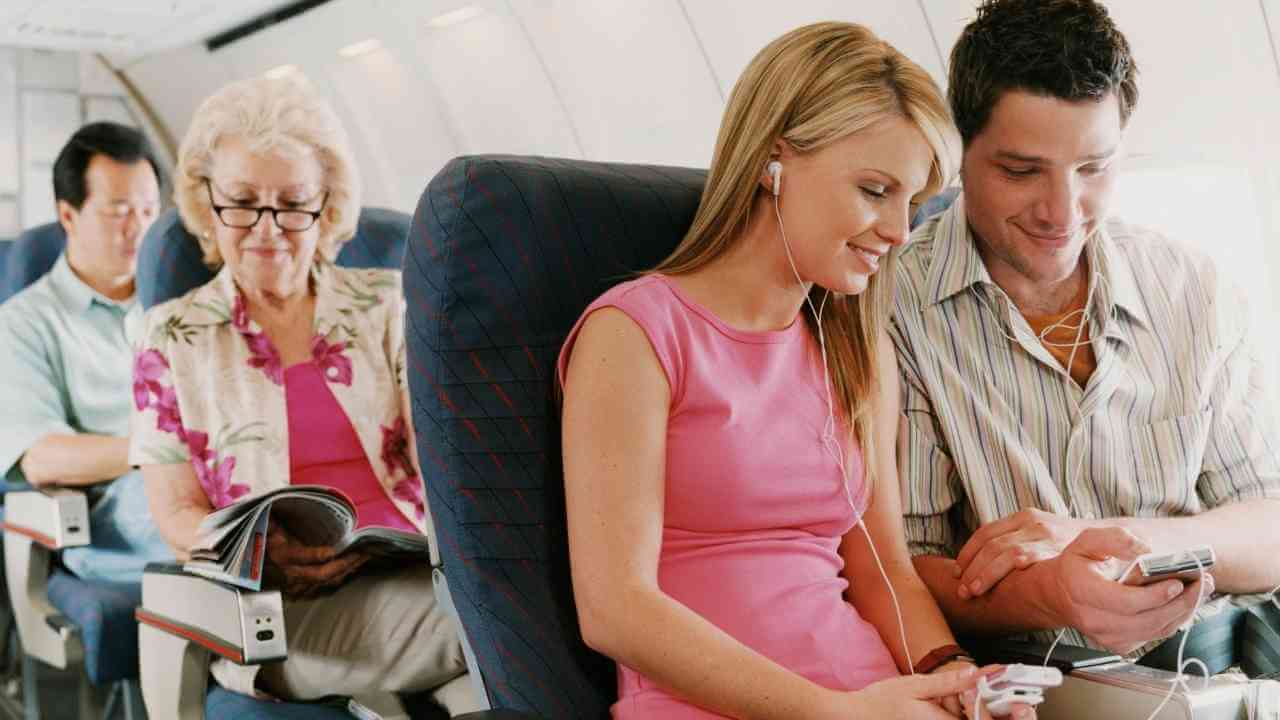 Two people sitting on an airplane looking at their cell phones