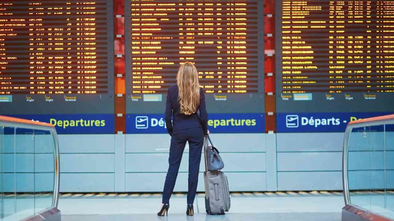 A person in a business suit standing in front of an airport departure board