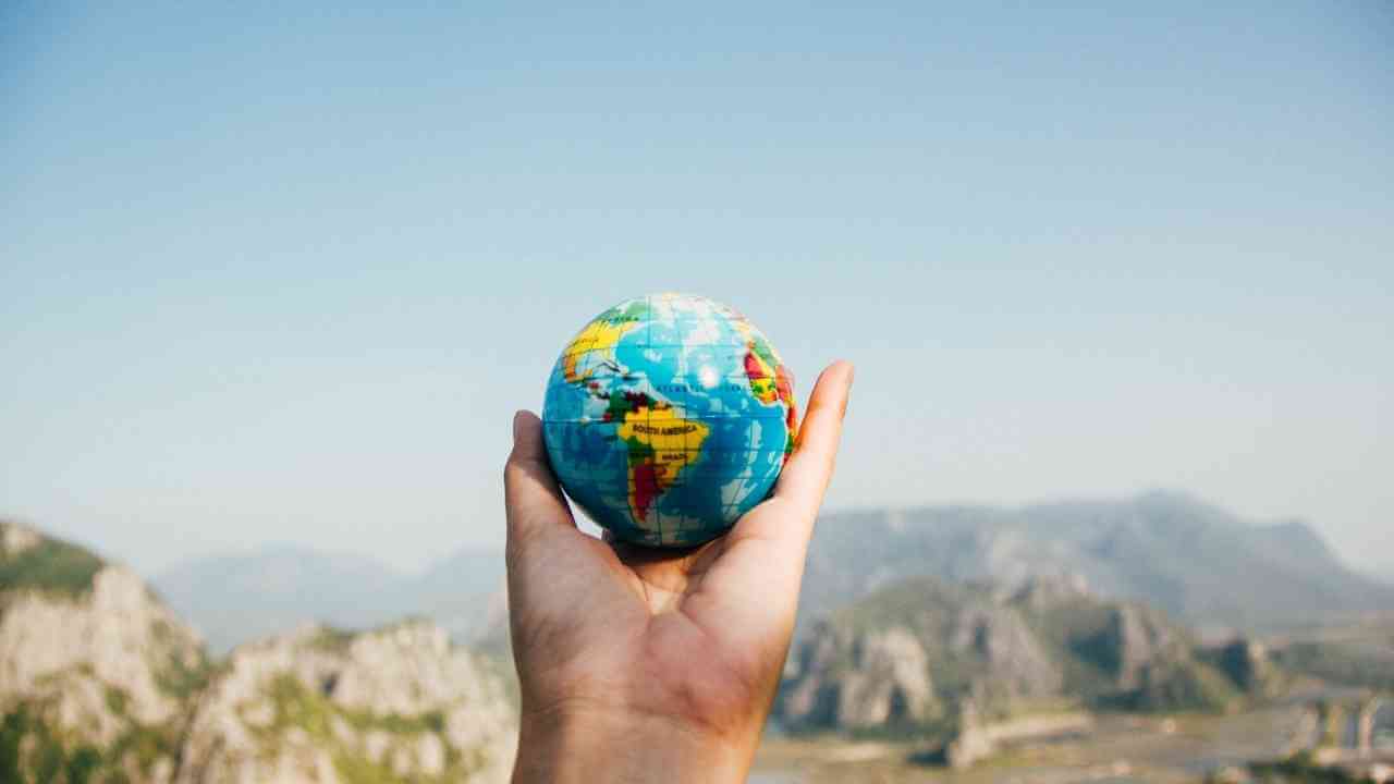 a person holding up a globe with mountains in the background