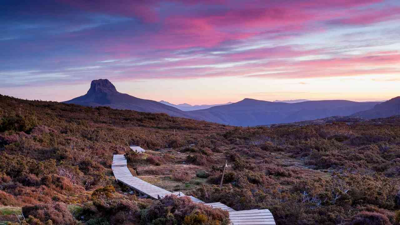 a wooden walkway leads to the top of a mountain at sunset