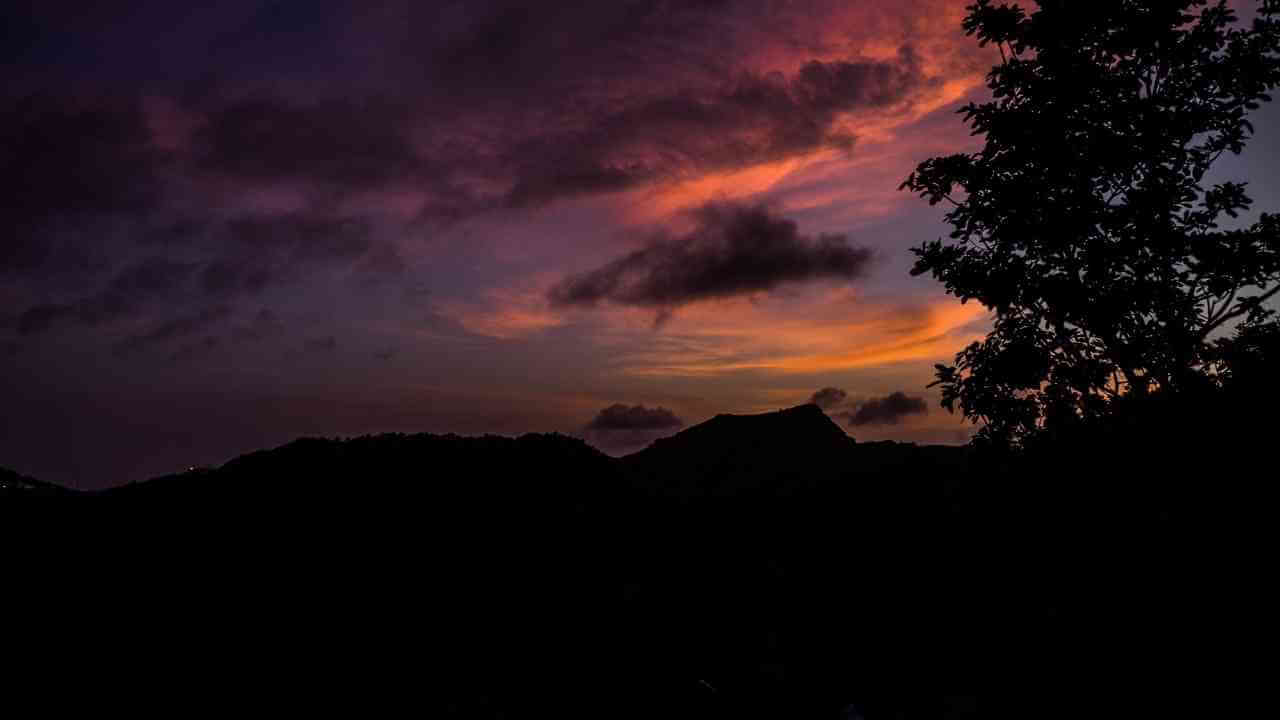 a sunset over a mountain range with a tree in the foreground