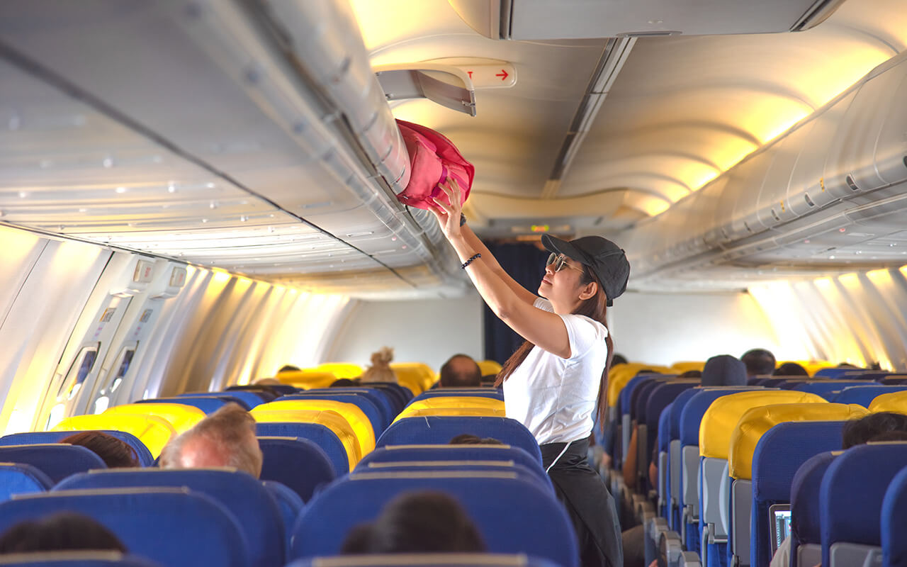 Woman placing bag into overhead bin on an airplane 