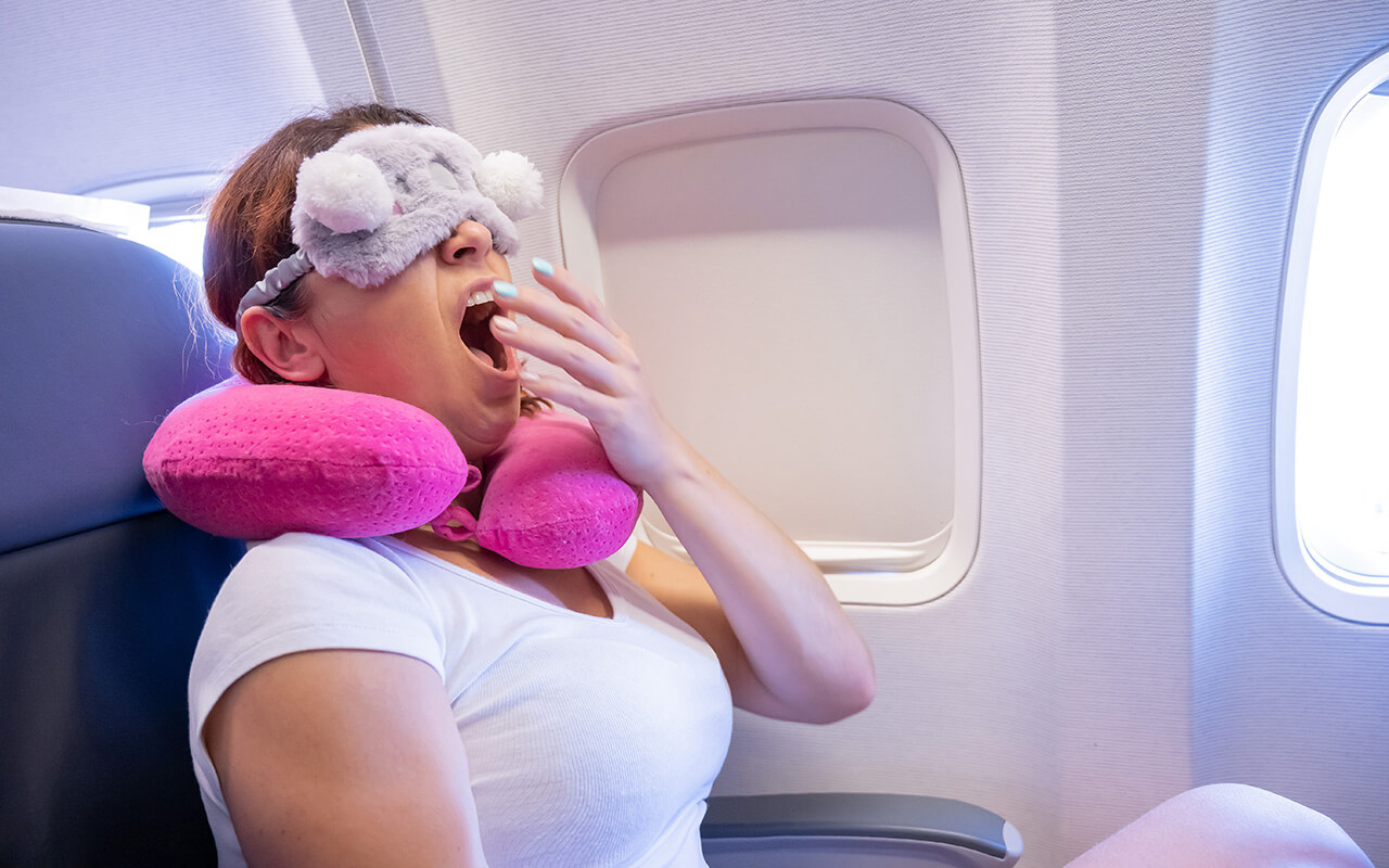 Woman on airplane wearing eye mask and neck pillow