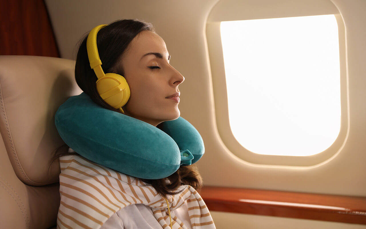 Woman sleeping on airplane wearing neck pillow 