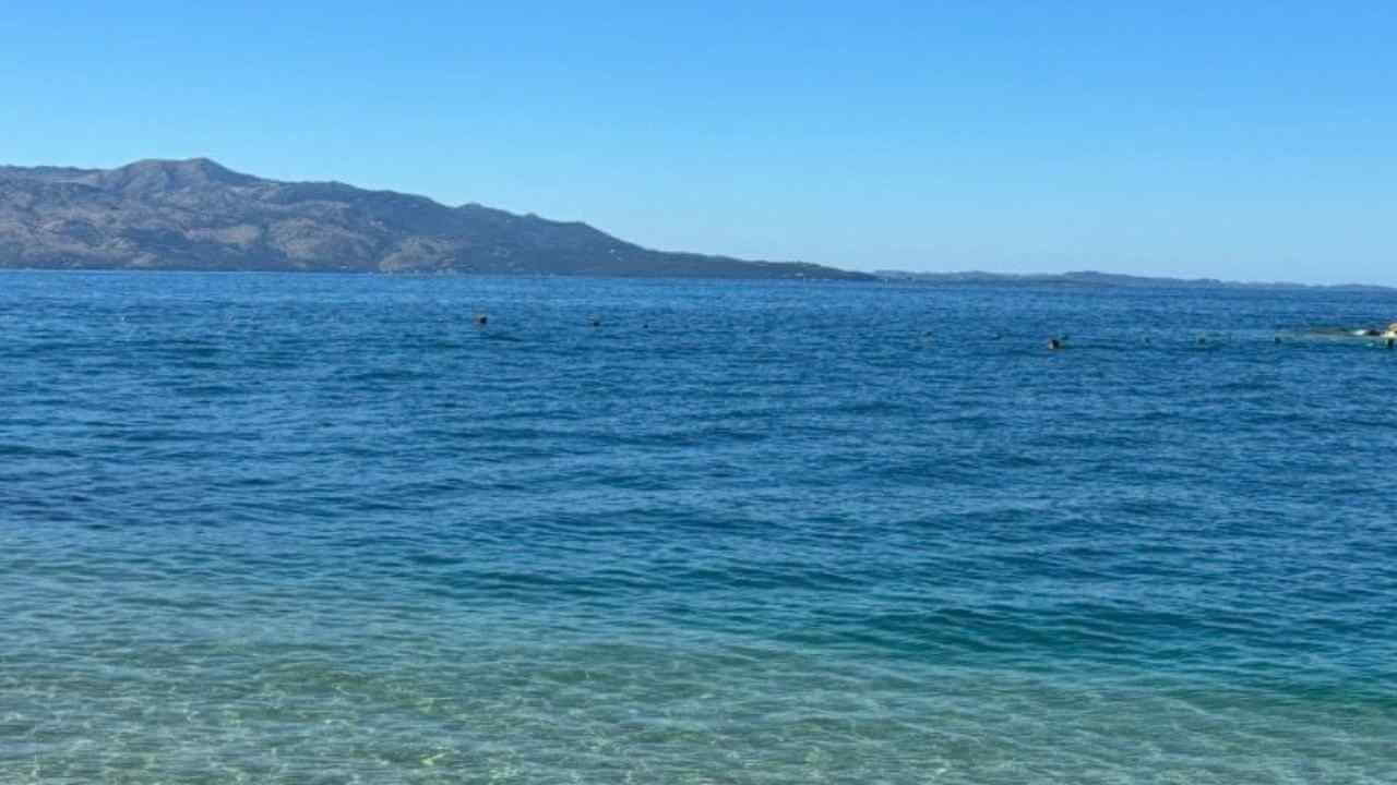 a body of water with rocks in the foreground and mountains in the background