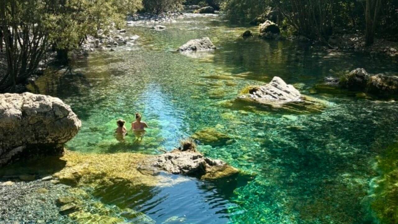 two people are swimming in the clear water of a river