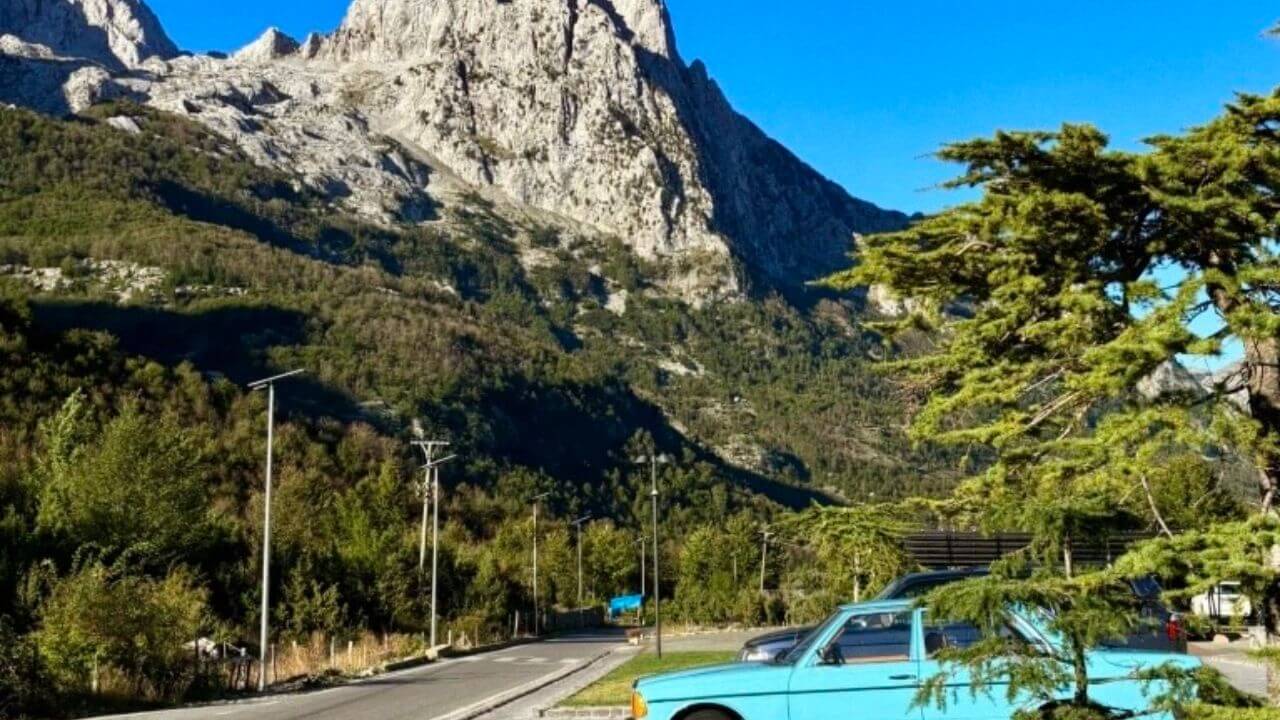 a blue car parked on the side of the road in front of a mountain