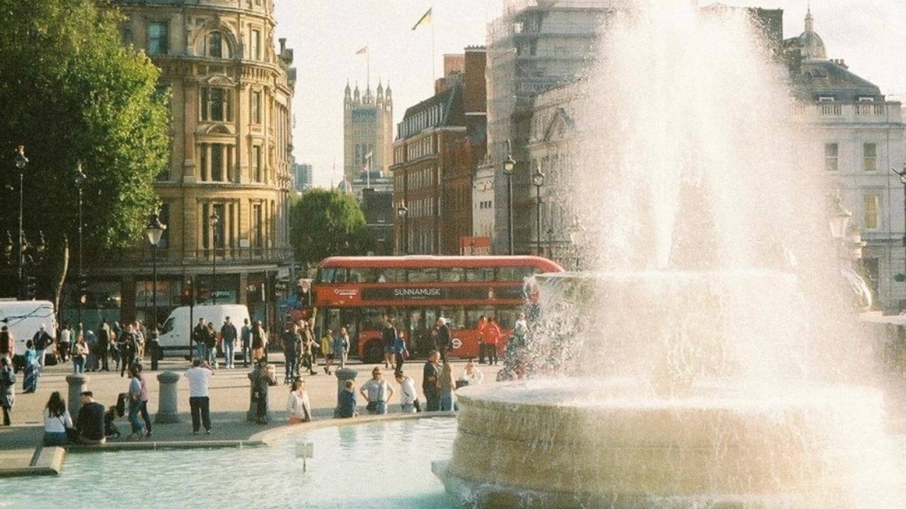 a fountain in the middle of a city with a red bus in the background