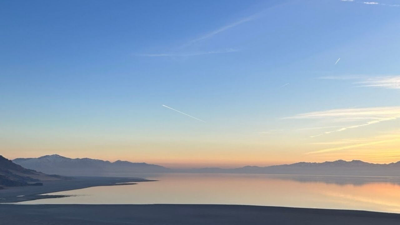 the sun is setting over a body of water with mountains in the background