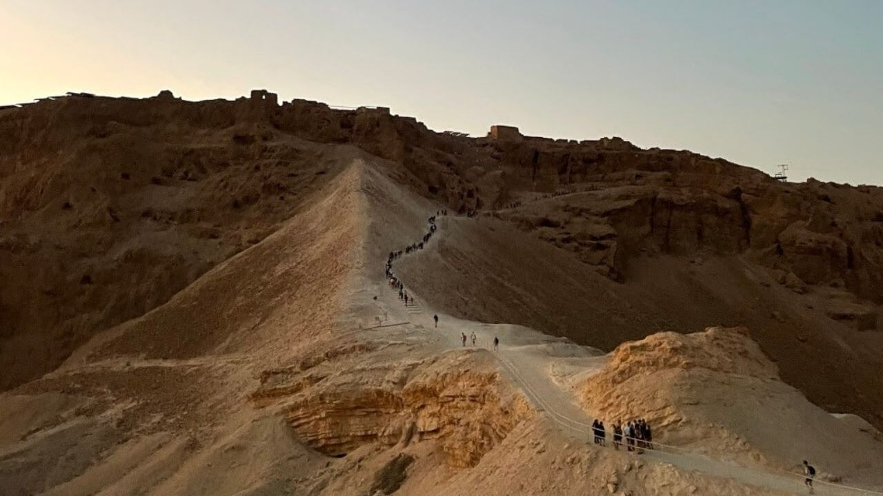 a group of people walking up a hill in the desert