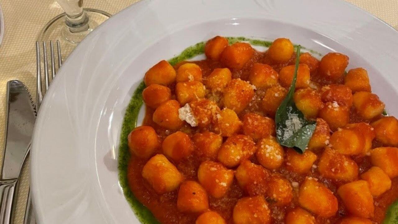 a plate of gnocchi on a table next to a glass of wine