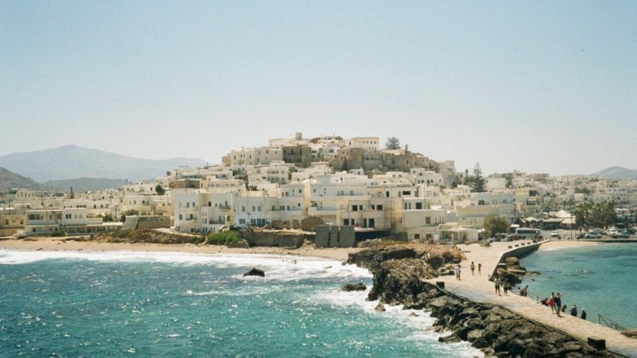 a view of a town on the coast with people walking on the beach