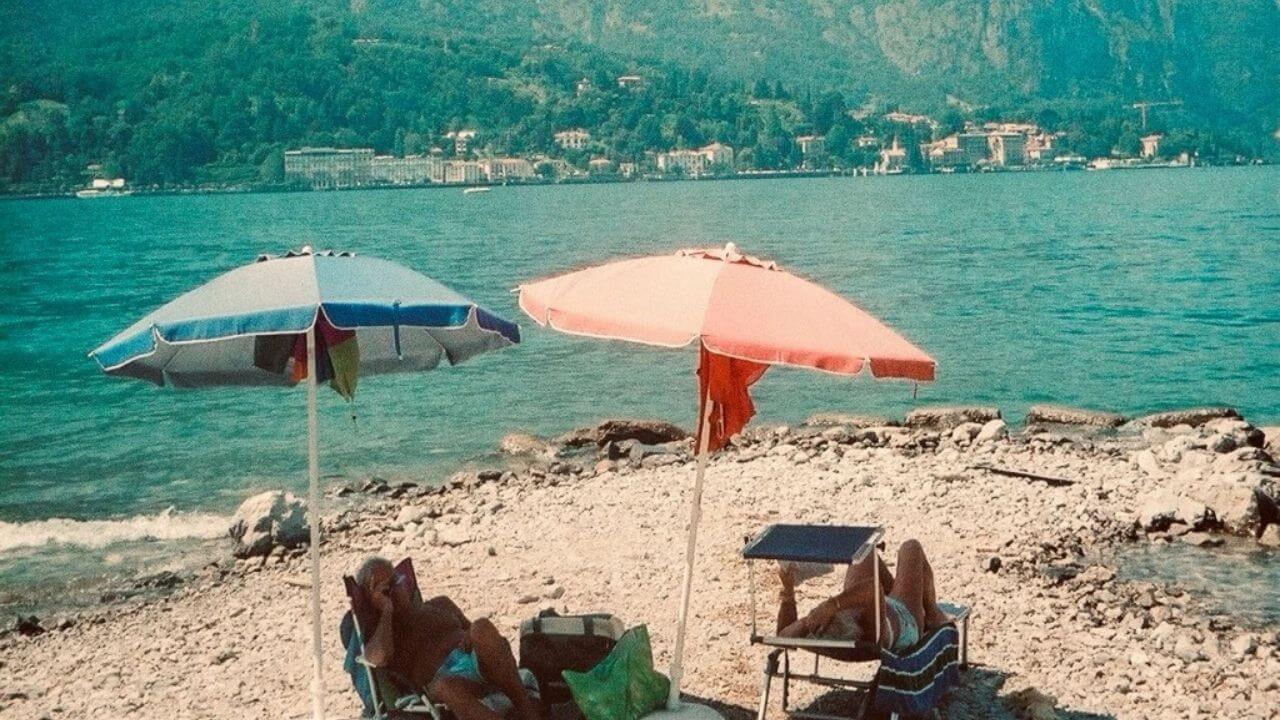 two people sitting under umbrellas on the beach with mountains in the background