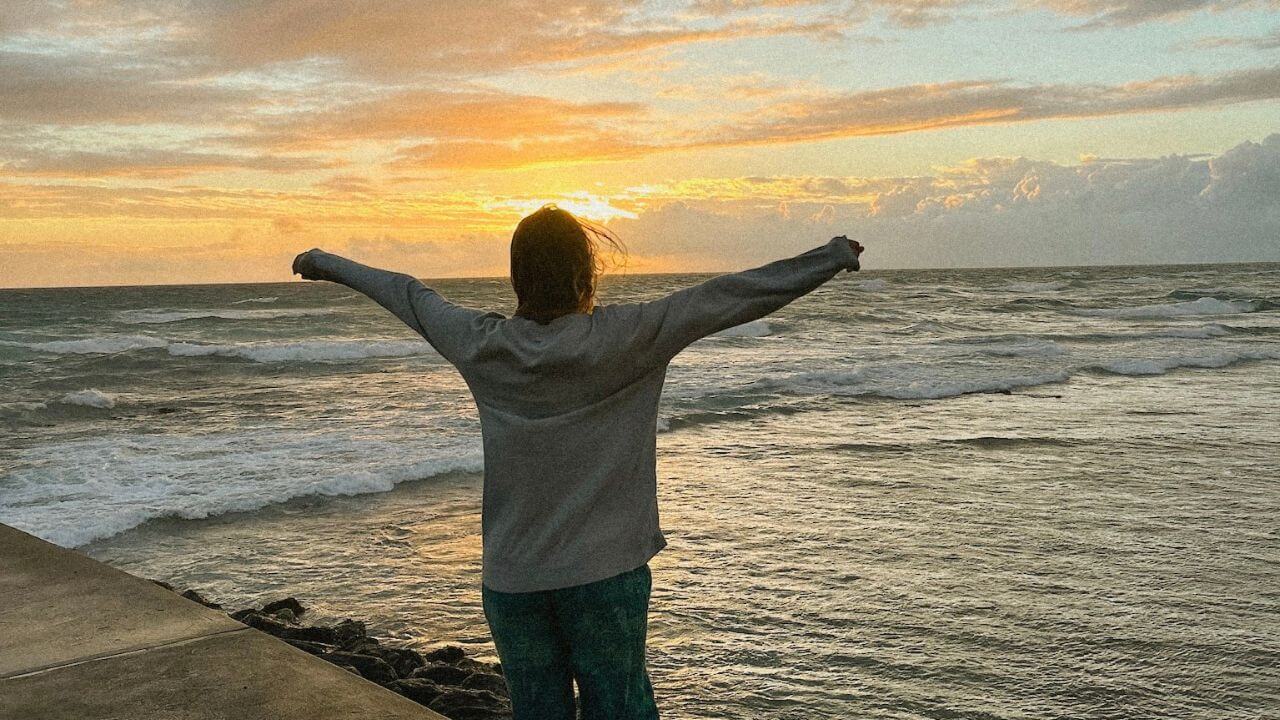 a person standing on the edge of a pier with their arms outstretched at sunset