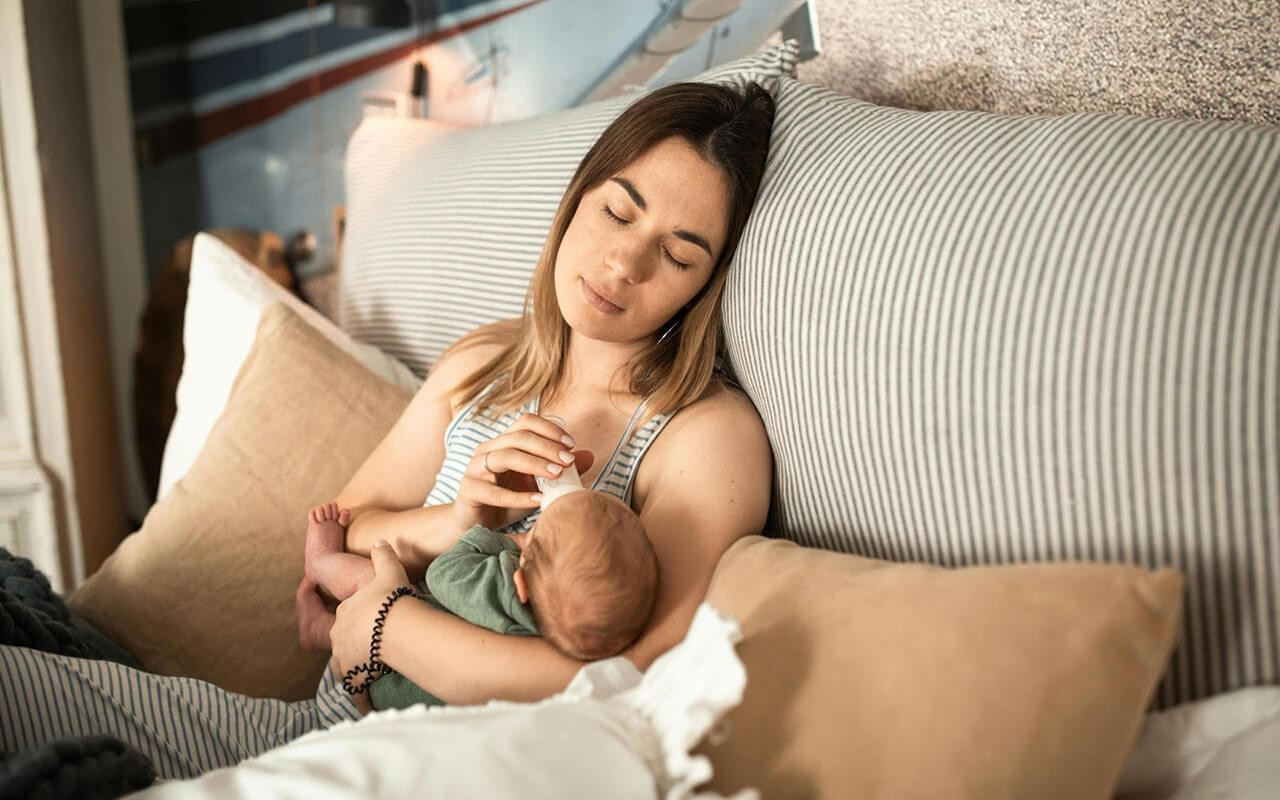 Woman with eyes closed feeding a baby from a bottle 