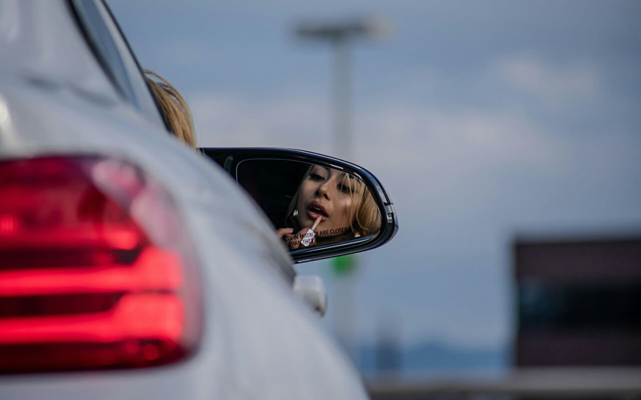 Woman applying lipgloss in a car mirror