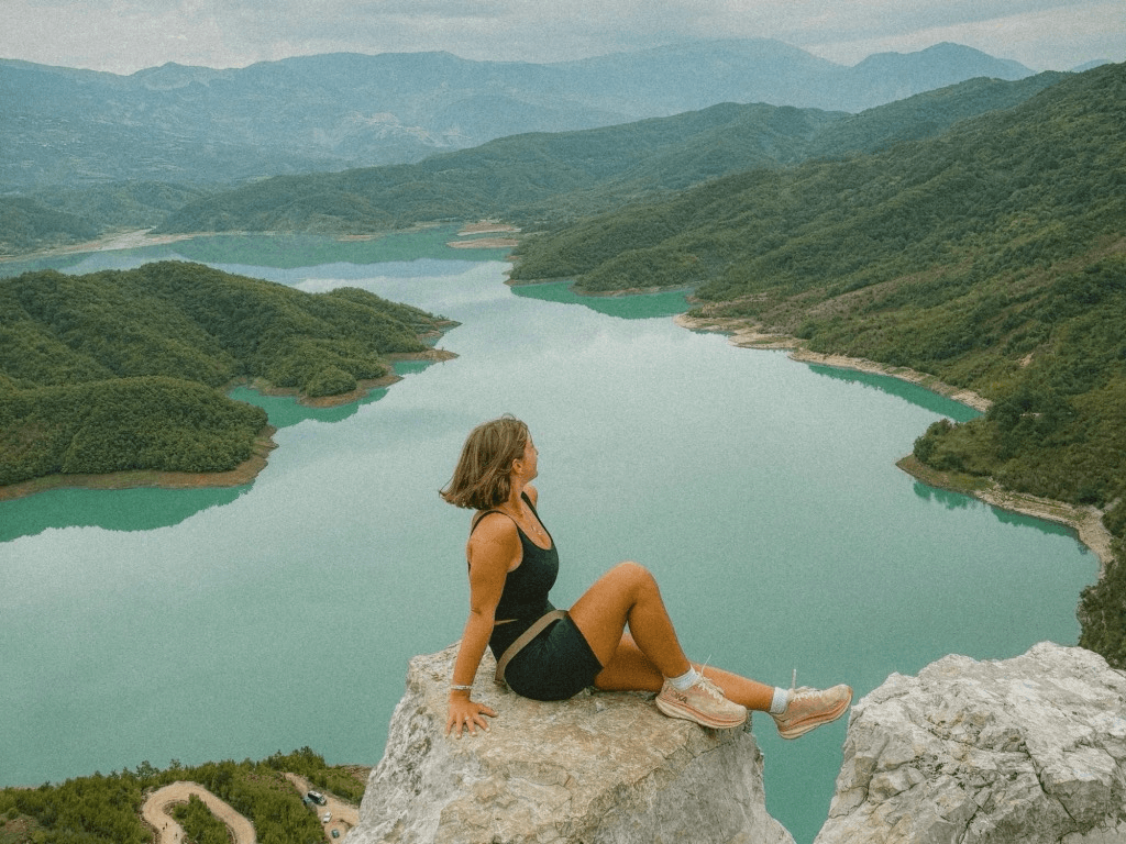 a person sitting on the edge of a cliff overlooking a lake