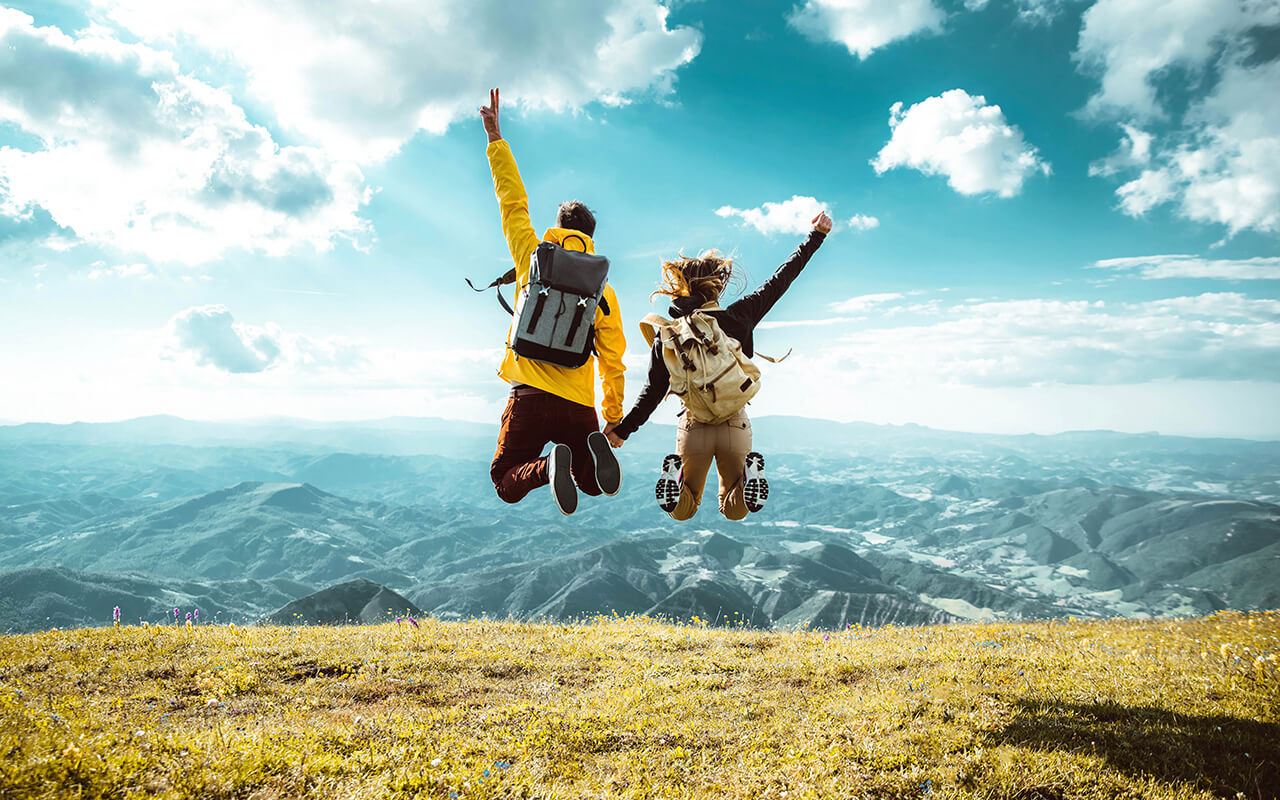 Hikers with backpacks jumping with arms up on top of a mountain