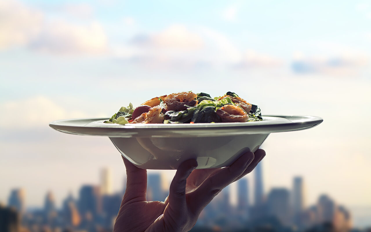 Waitress woman hand with plate of salad on skyscrapers of New York city background. 