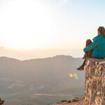 Beautiful woman sitting on an edge during sunset with mountains