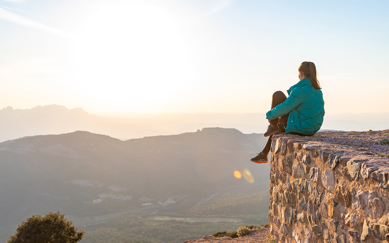 Beautiful woman sitting on an edge during sunset with mountains