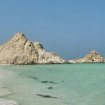 a sandy beach with rocks in the ocean and clear water