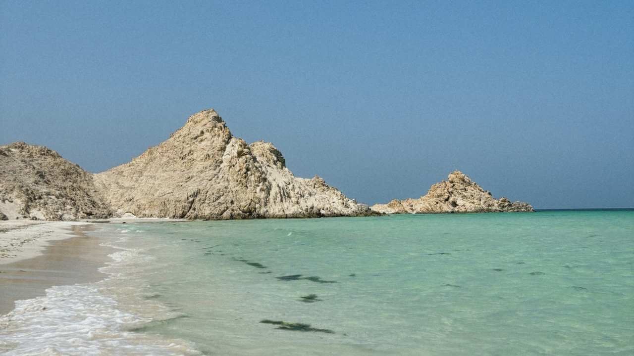 a sandy beach with rocks in the ocean and clear water