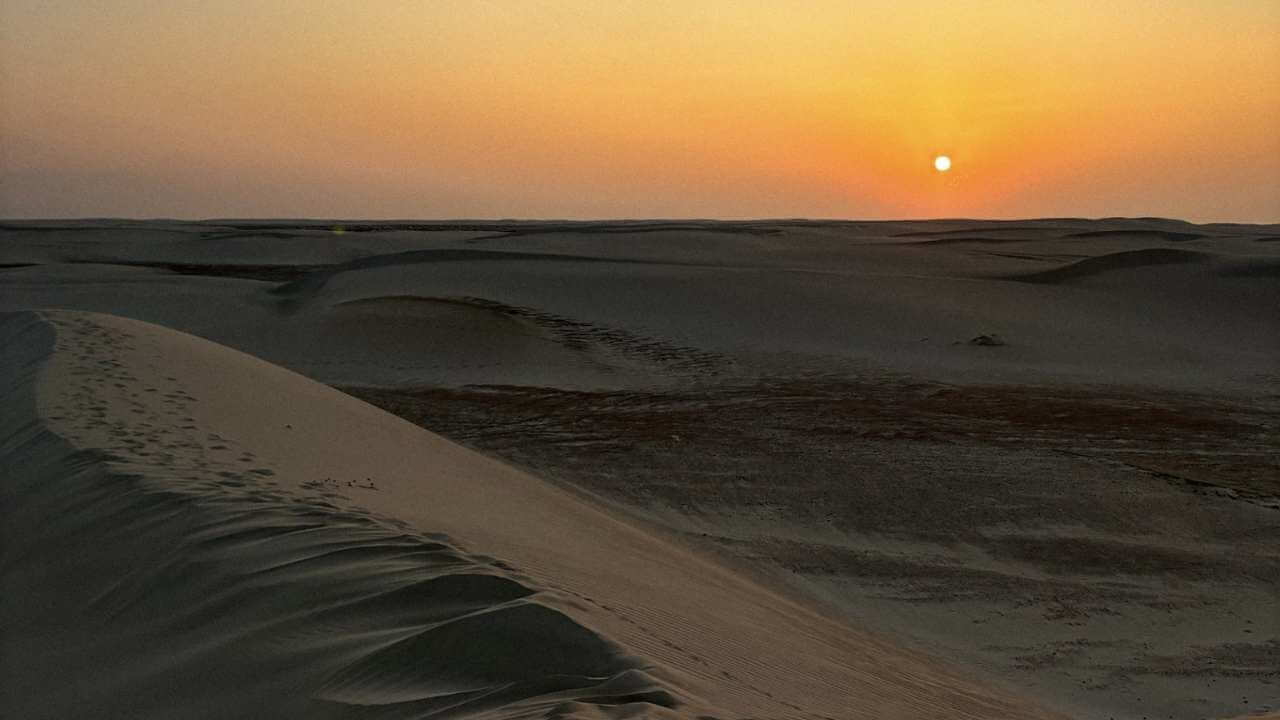 the sun is setting over the sand dunes in the desert