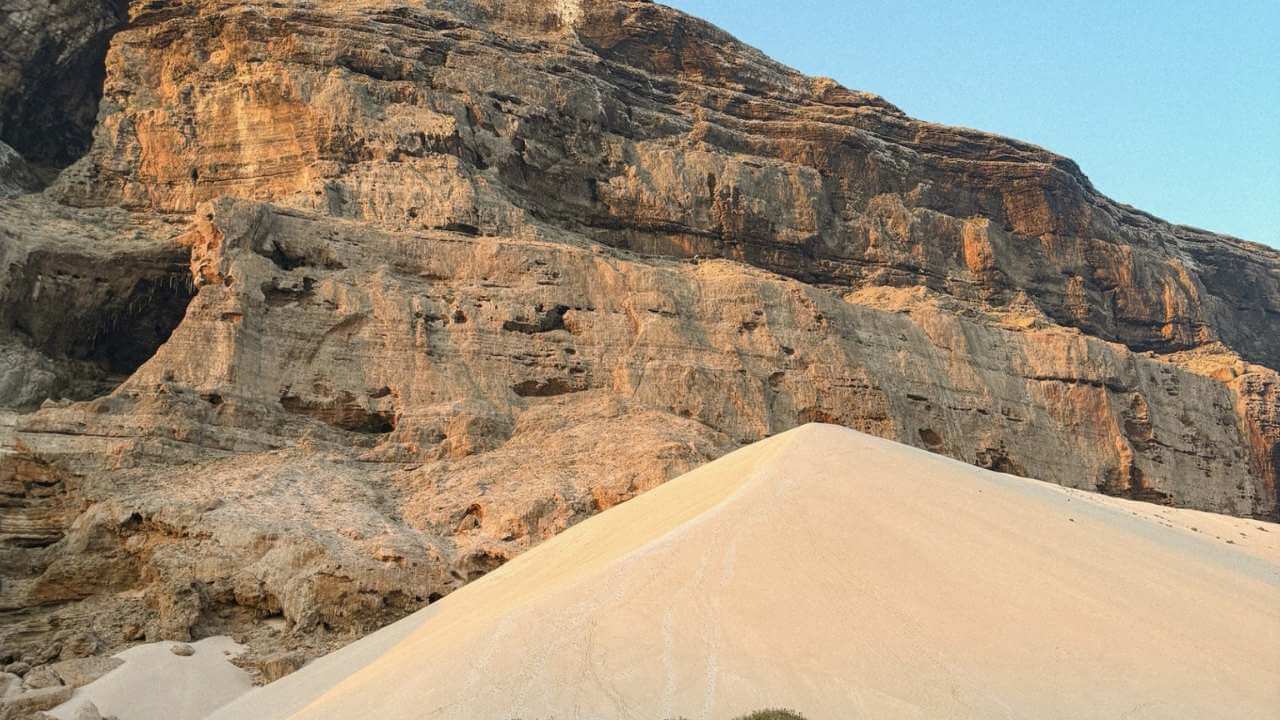 a sand dune in the middle of the desert with a mountain in the background