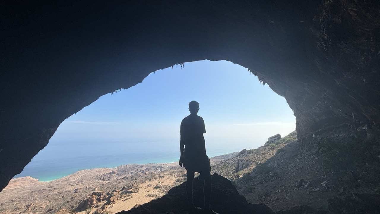 a person standing inside of a cave looking at the ocean