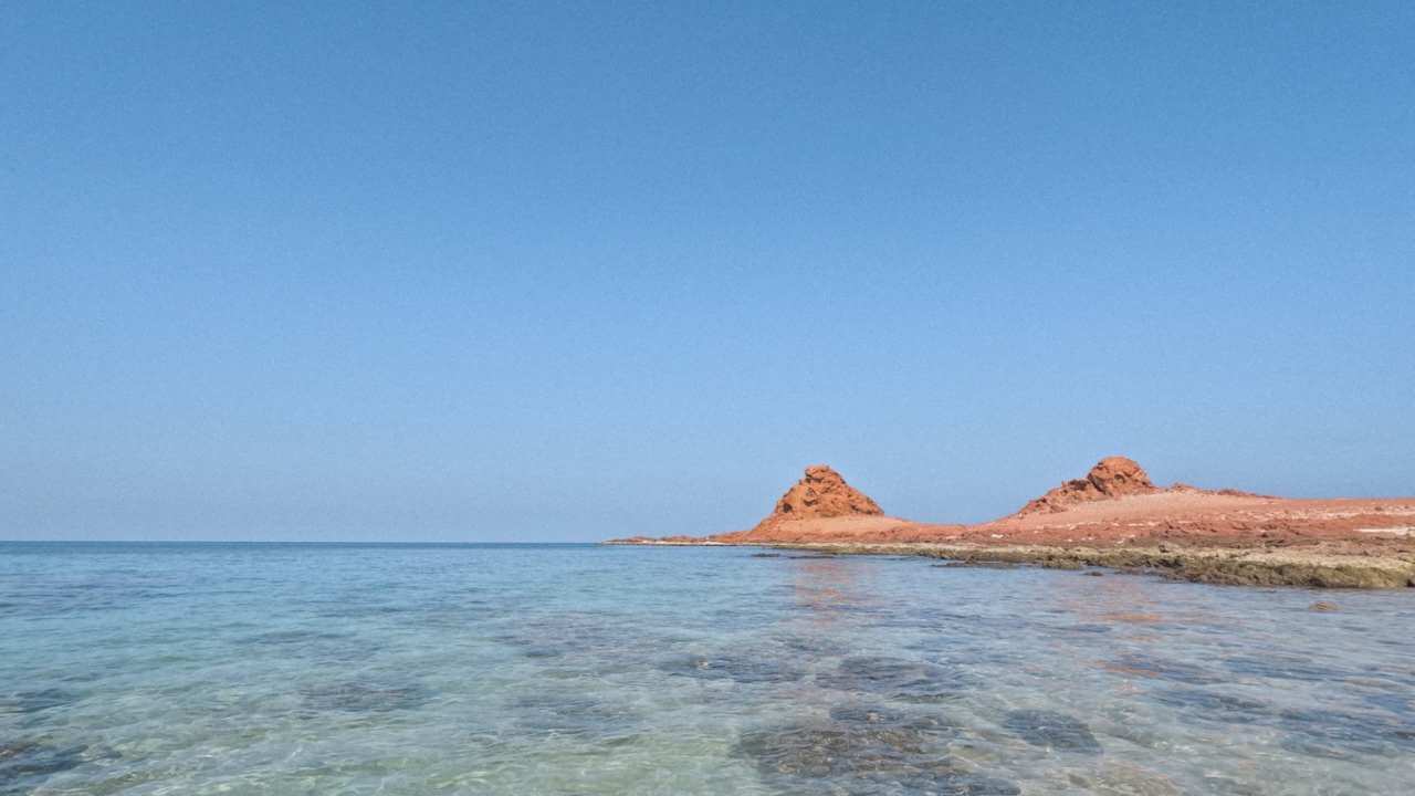 red rock formations in the ocean near a clear body of water