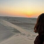 a person standing in front of a sand dune at sunset