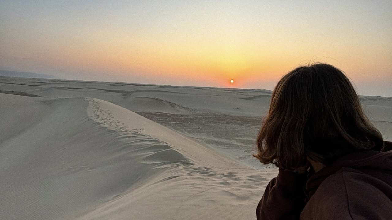 a person standing in front of a sand dune at sunset