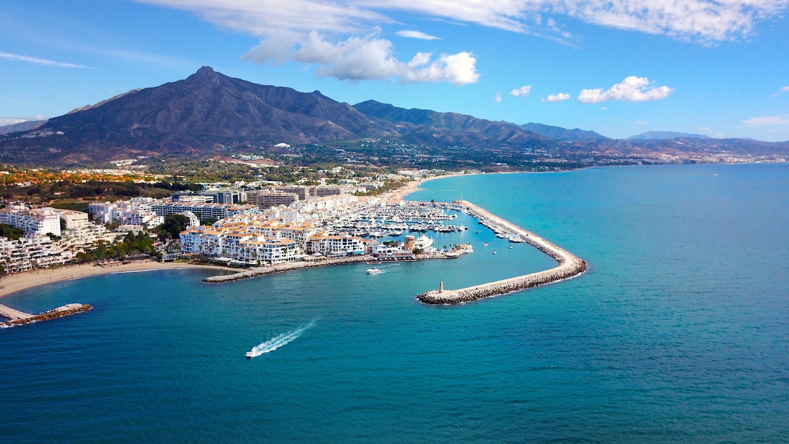 aerial view of luxury yachts in Puerto Banús marina, habor wall and the lighthouse Faro Puerto Banús, prominent Pico de la Concha mountain behind, Marbella, Malaga, Costa del Sol, Spain