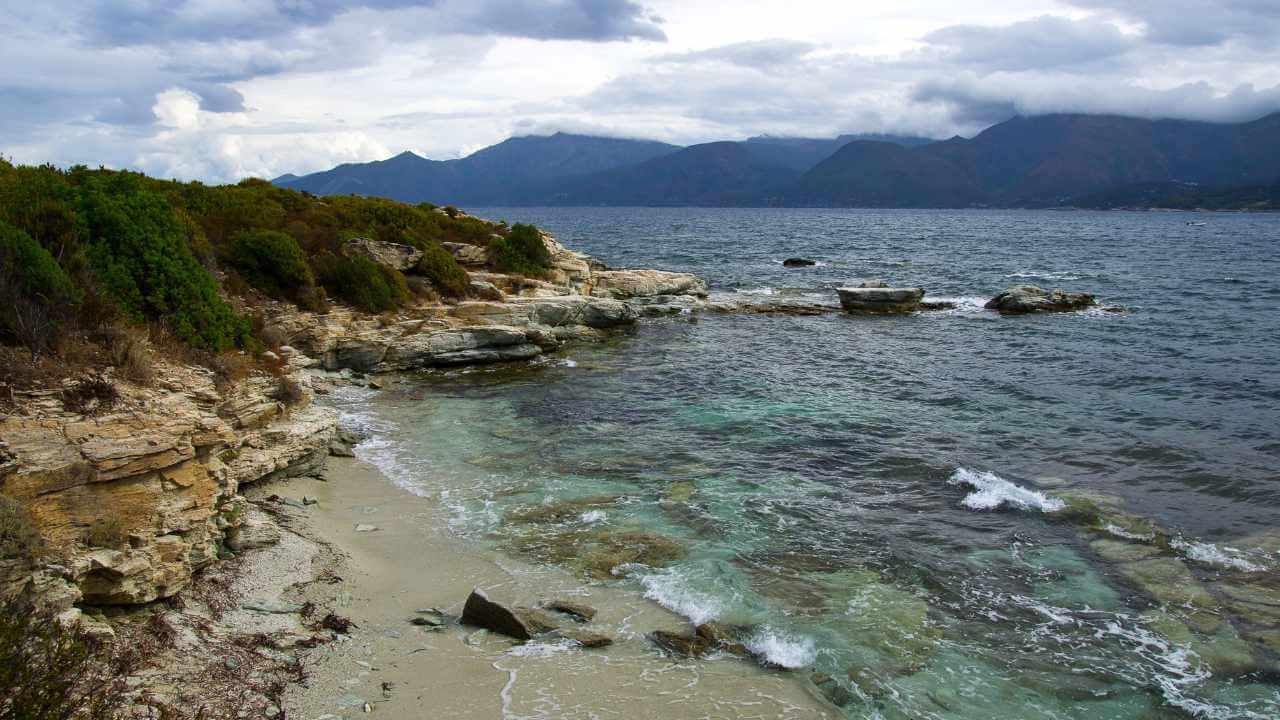 a view of a rocky shoreline with water and mountains in the background