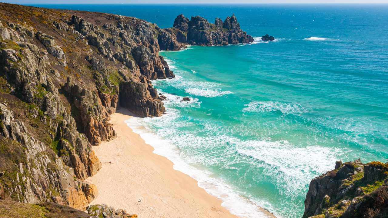 a view of a sandy beach and rocky cliffs on a sunny day