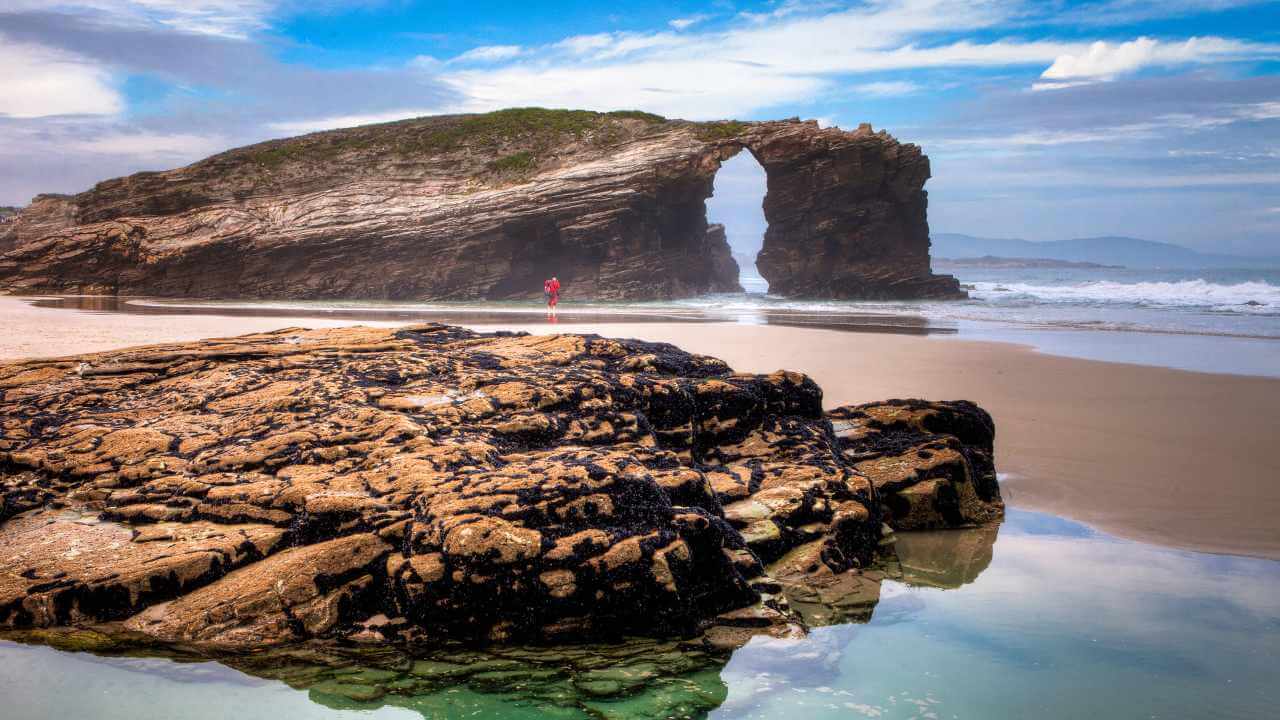 a rock formation on the beach with a person standing in front of it